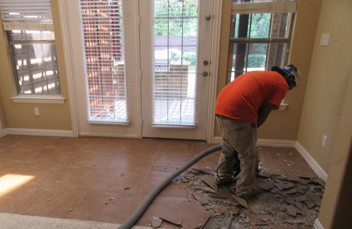 Worker in orange t-shirt using equipment to remove tiles.